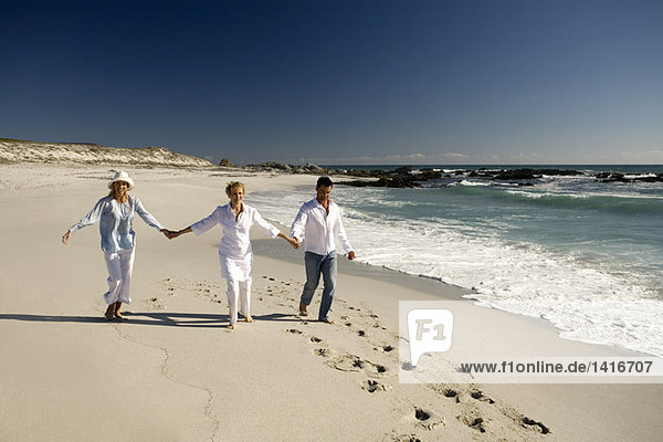 Ehepaar und Seniorin halten sich am Strand an den Händen.