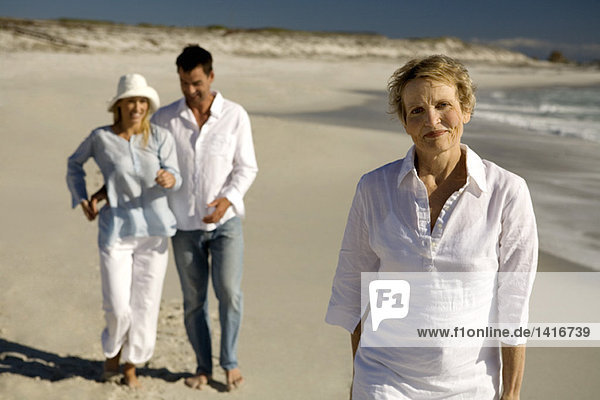 Couple embracing and senior woman waking on the beach