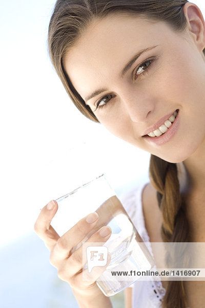 Porträt einer jungen Frau,  die ein Wasserglas hält,  im Freien
