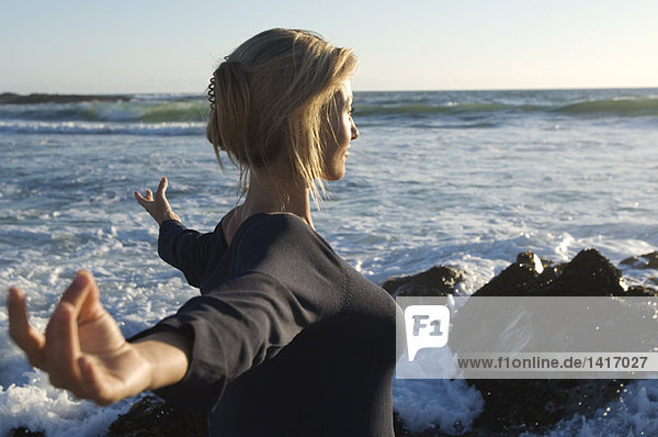 Junge Frau in Yogahaltung am Strand  im Freien