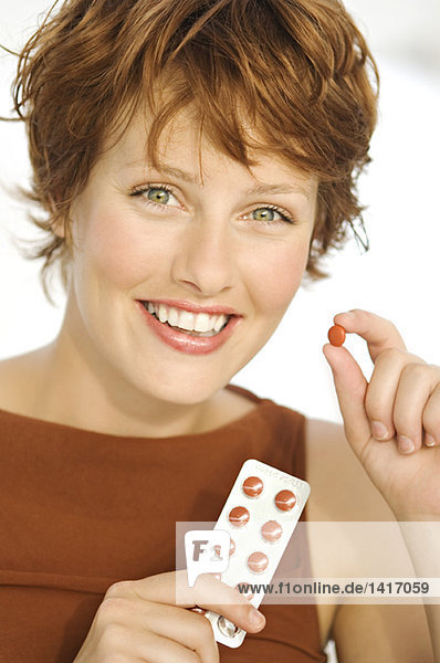 Porträt einer jungen lächelnden Frau mit Pillen