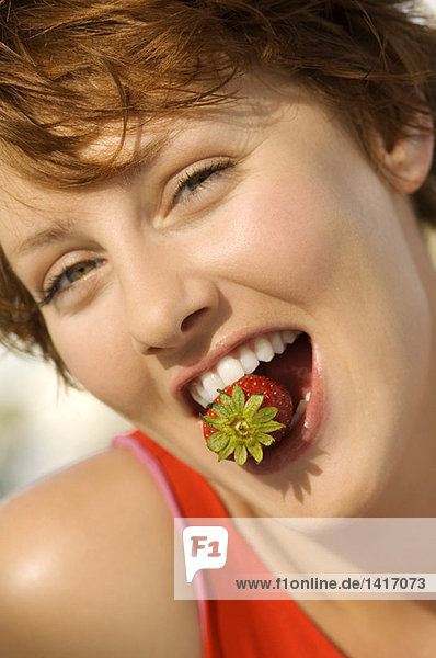 Porträt einer jungen Frau mit Erdbeere zwischen den Zähnen
