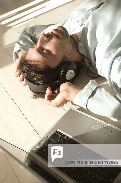 Junger Mann auf dem Boden liegend  Musik hören mit Laptop