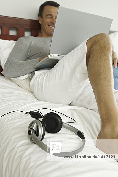Mann auf dem Bett liegend  mit Laptop