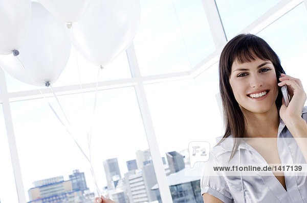Portrait of a smiling woman phoning  holding white balloons