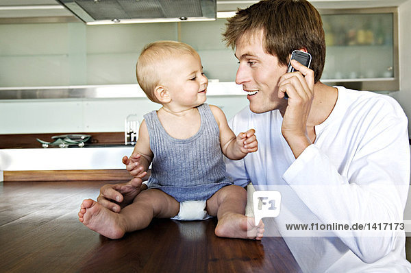 Young man phoning  embracing baby