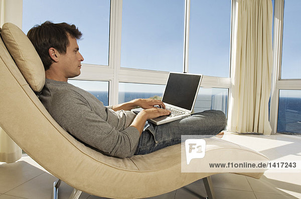 Junger Mann mit Laptop im Sessel
