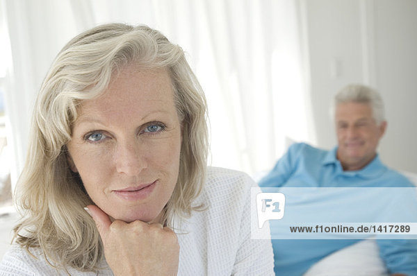 Couple in bedroom  woman looking at camera  man lying in background