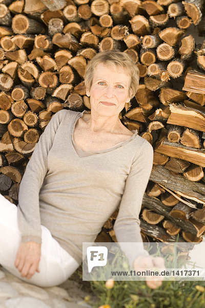 Seniorin sitzend am Holzhaufen