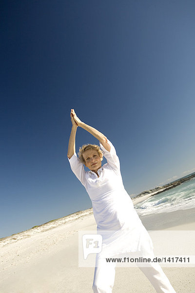 Senior woman doing yoga on the beach