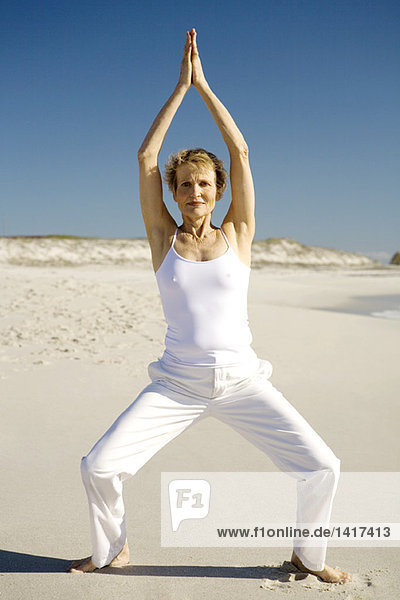 Senior woman doing yoga on the beach