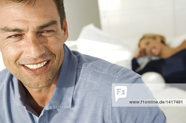 Portrait of smiling man  woman lying on bed in background