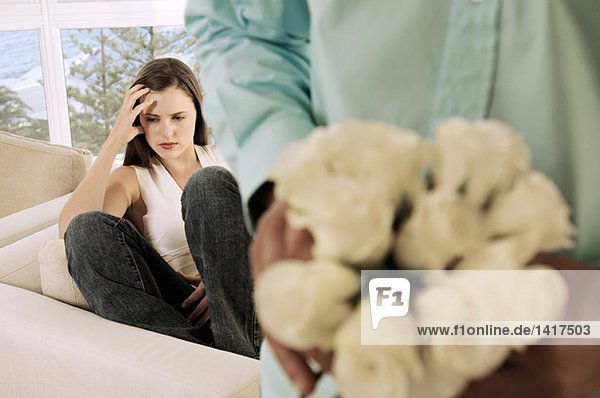 Man hiding bunch of flowers behind his back  facing sulking woman