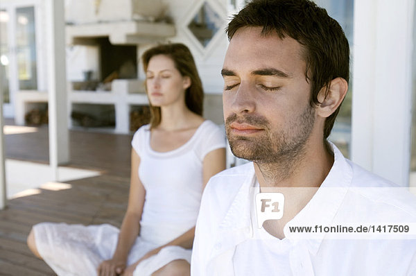 Couple sitting cross-legged on wooden terrace  eyes closed