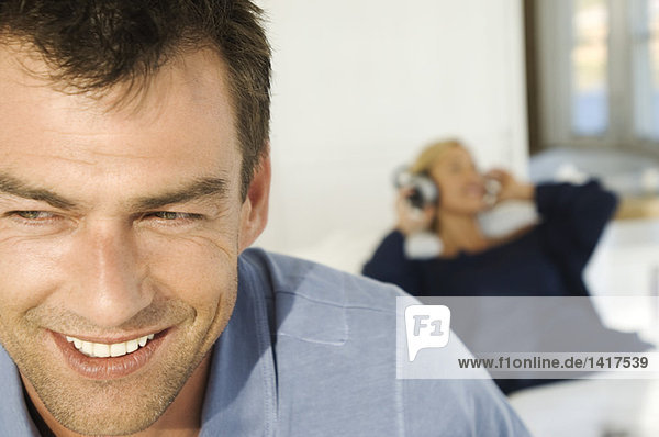 Porträt eines lächelnden Mannes  Frau beim Musikhören im Hintergrund