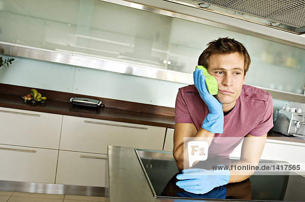 Young man in kitchen  leaning sponge against his cheek