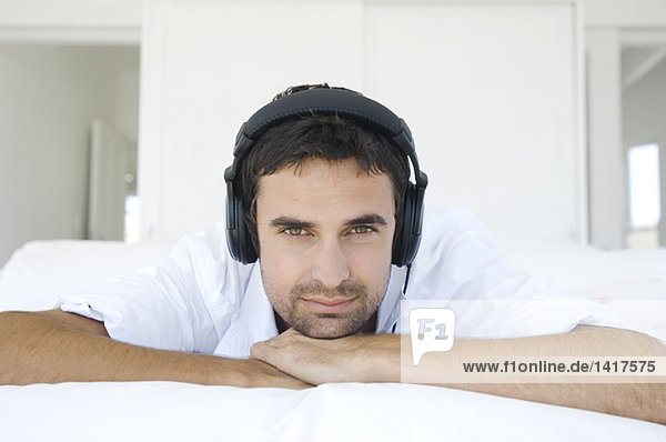 Young man lying on bed  listening to music with headphones