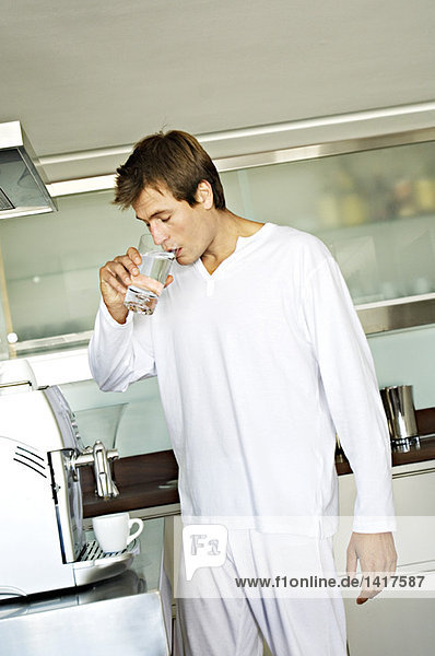 Junger Mann trinkt Wasser in der Küche