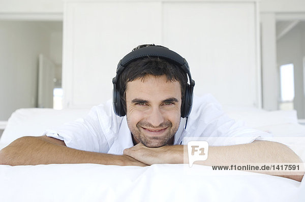 Young smiling man lying on bed  listening to music with headphones