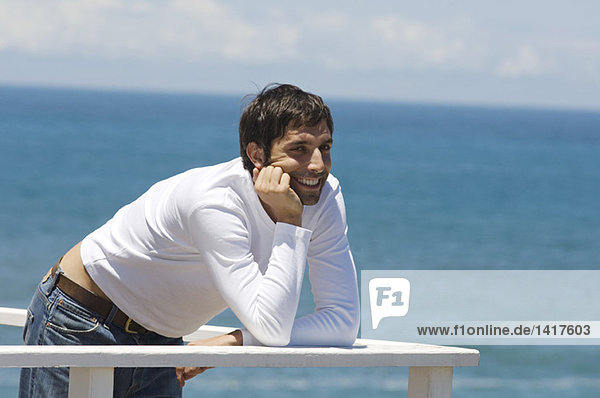 Junger lächelnder Mann an der Balustrade lehnend  Meer im Hintergrund