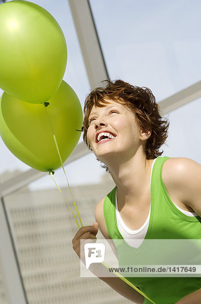 Porträt einer jungen lächelnden Frau mit grünen Luftballons