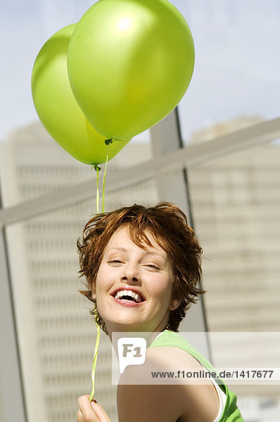 Porträt einer jungen Frau mit grünen Luftballons