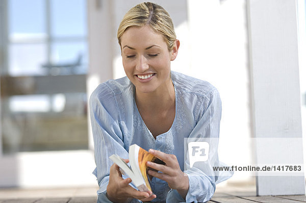 Junge Frau beim Lesen eines Buches  auf der Terrasse liegend