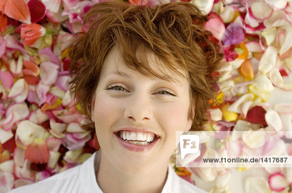 Porträt einer jungen lächelnden Frau  auf Blütenblättern liegend