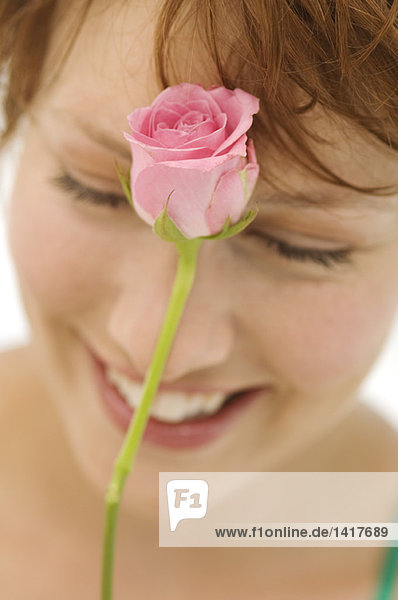 Porträt einer jungen lächelnden Frau mit Rose vor dem Gesicht