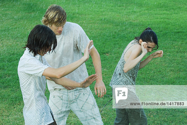 Gruppe junger Freunde im Wasserspray stehend  nass werdend