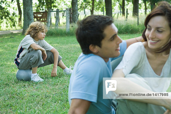 Familie sitzt auf Gras im Freien  Fokus auf Junge sitzt auf Ball im Hintergrund