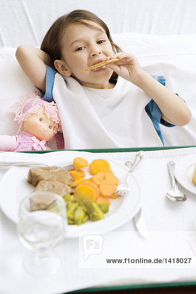 Mädchen im Krankenhausbett liegend mit Essenstablett vor sich  Kekse essend