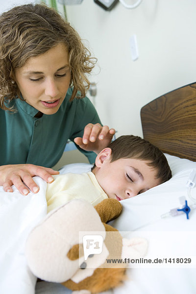 Junge schläft im Krankenhausbett  Praktikant schaut dem Jungen über die Schulter