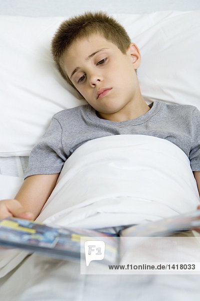 Kranker Junge liegt im Bett und liest Comicbuch