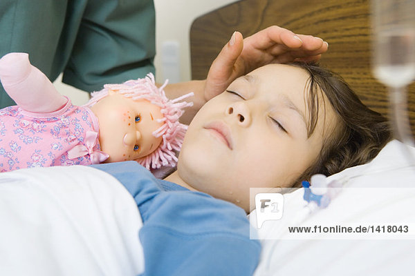Girl sleeping in hospital bed  woman's hand posed over girl's forehead