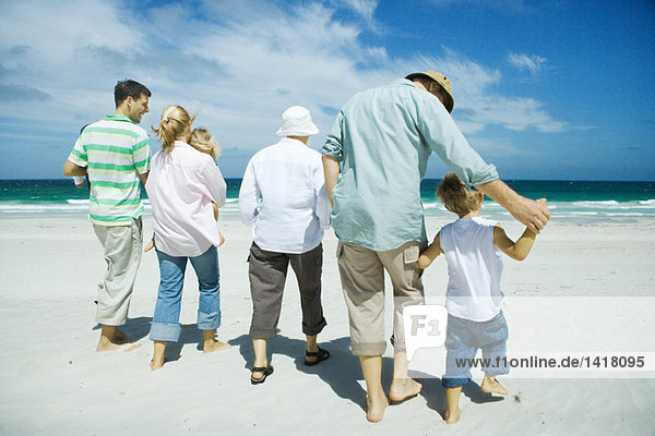 Three generation family walking on beach  rear view