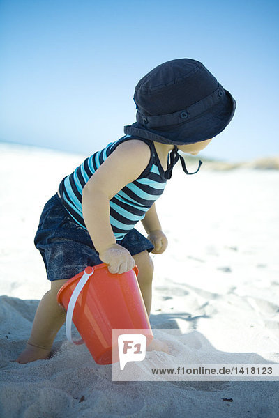 Kind am Strand stehend mit Sandeimer