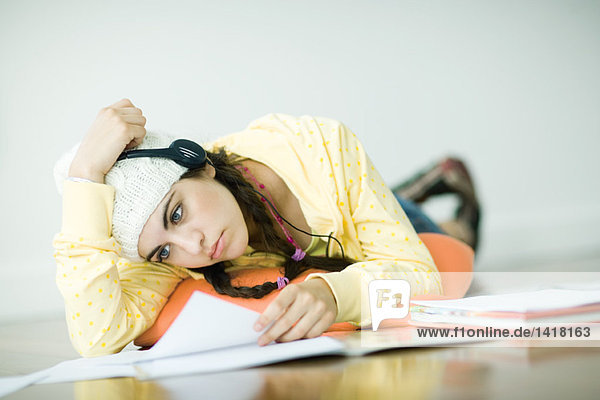Young woman lying on floor  wearing headphones and studying