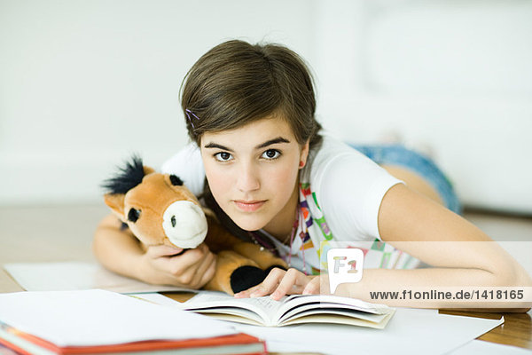 Teen girl lying on floor  doing homework  holding stuffed animal  looking at camera