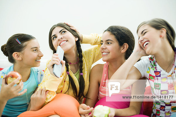 Four young female friends sitting together  smiling  snacking