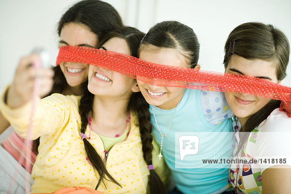 Vier junge Freundinnen halten einen Schal vor die Augen  eine fotografiert mit dem Handy.