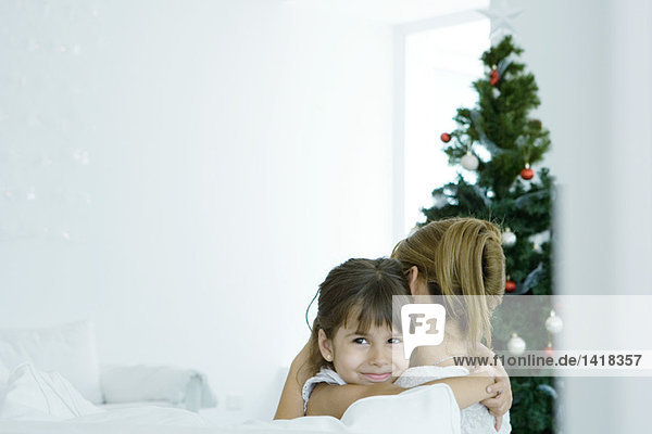 Mädchen umarmende Mutter am Weihnachtsbaum
