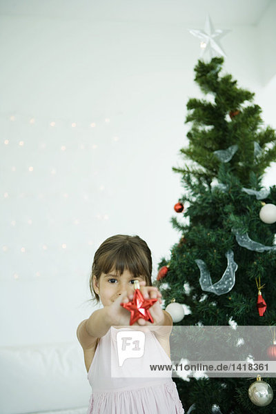 Girl holding out star decoration in front of Christmas tree