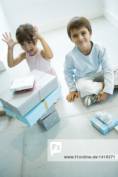 Zwei Kinder sitzen auf dem Boden mit einem Stapel von Geschenken.