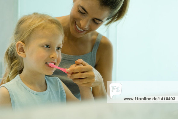 Mutter und Tochter putzen gemeinsam die Zähne des Mädchens