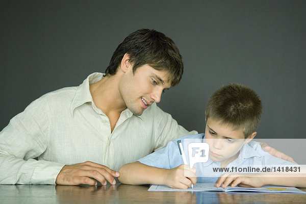 Vater und Sohn  Mann schaut dem Jungen über die Schulter  während er Hausaufgaben macht.