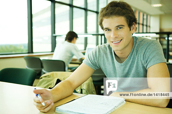 Männlicher Student sitzt am Tisch und lächelt vor der Kamera.