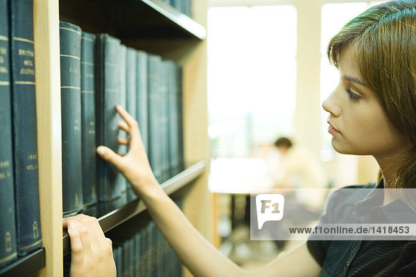 Weibliche Studentin nimmt Buch aus dem Regal in der Bibliothek