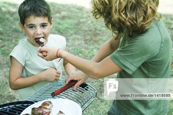 Junge füttert gegrilltes Fleisch an jüngeren Jungen