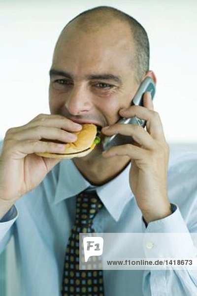 Mann isst Hamburger und benutzt Handy